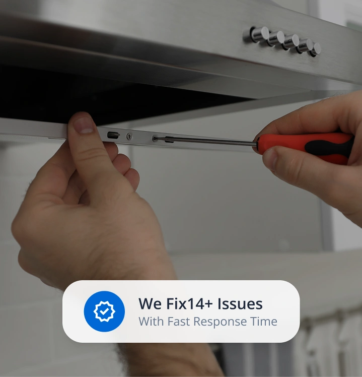 Hands tightening a screw on a stainless steel kitchen range hood with a red-handled screwdriver