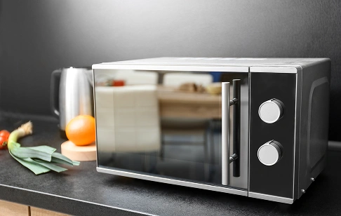 Stainless steel microwave on a kitchen counter with vegetables (celery and leek) nearby.